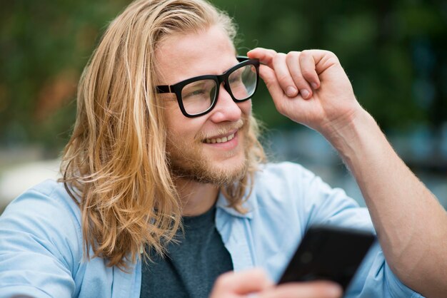 Front view of smiley man outdoors with smartphone