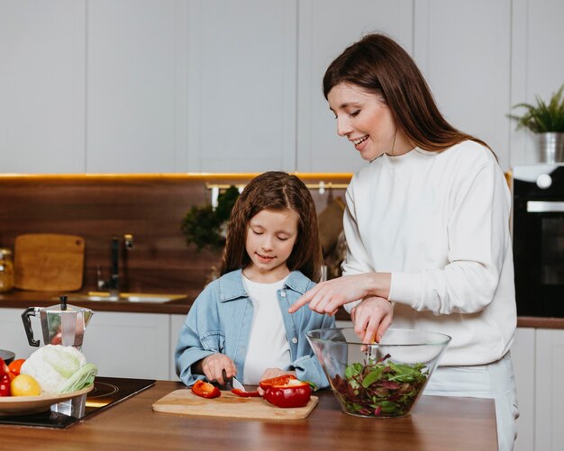 Front view of smiley mother and daughter preparing food in the kitchen