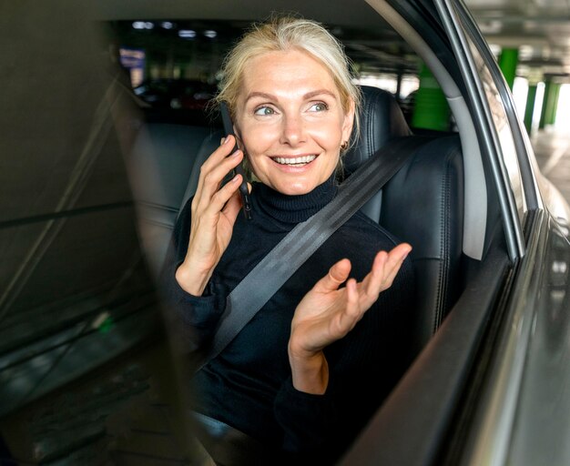 Front view of smiley older business woman talking on the phone in car