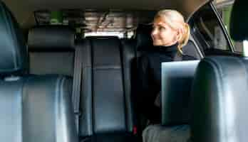 Free photo front view of smiley older business woman working on laptop in car