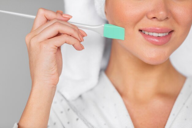 Front view of smiley woman in bathrobe applying skincare