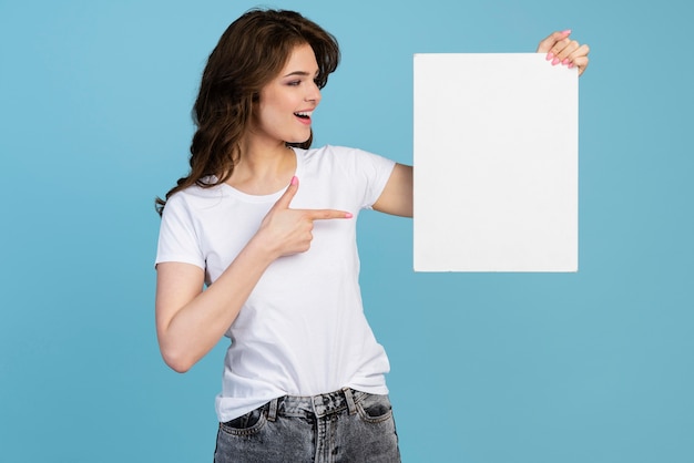 Front view of smiley woman holding and pointing at blank placard