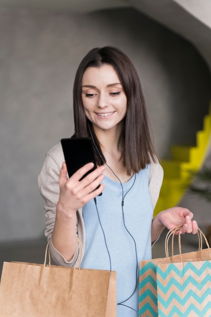 Front view of smiley woman holding smartphone and paper bags