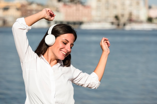 Free Photo front view of smiley woman listening to music on headphones at the beach