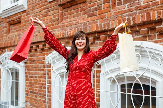 Front view of smiley woman posing with multiple shopping bags