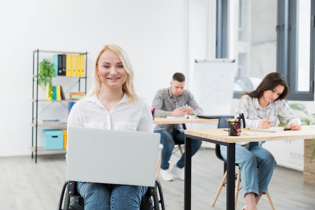 Free photo front view of smiley woman in wheelchair posing with laptop at work