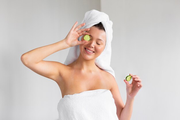 Front view of smiley woman with towel on head holding cucumber slices