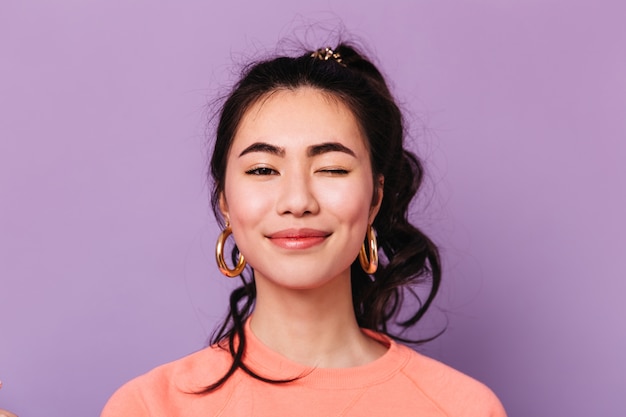 Front view of smiling asian woman in earrings. Studio shot of joyful chinese lady isolated on purple background.