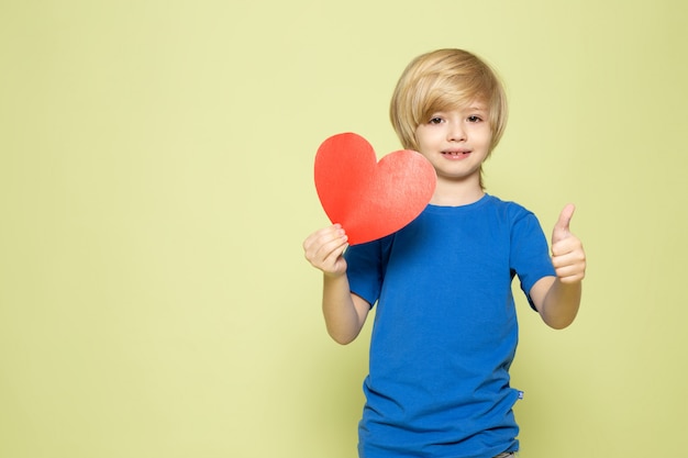 Free Photo a front view smiling boy in blue t-shirt holding heart shaped figure on the stone colored space