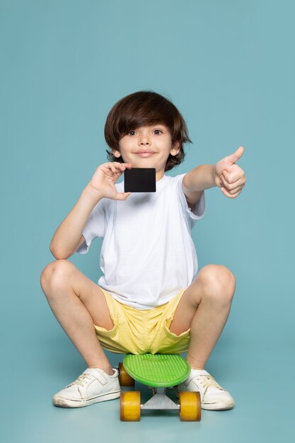 Free Photo a front view smiling boy in white t-shirt and yellow jeans riding green skateboard on the blue space