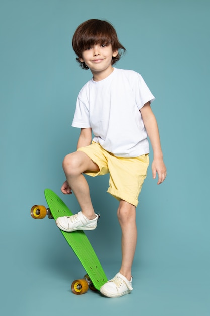 A front view smiling cute child sweet adorable in white t-shirt holding skateboard on the blue space