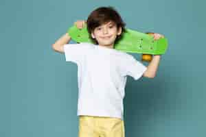 Free photo a front view smiling cute kid in white t-shirt holding skateboard on the blue floor