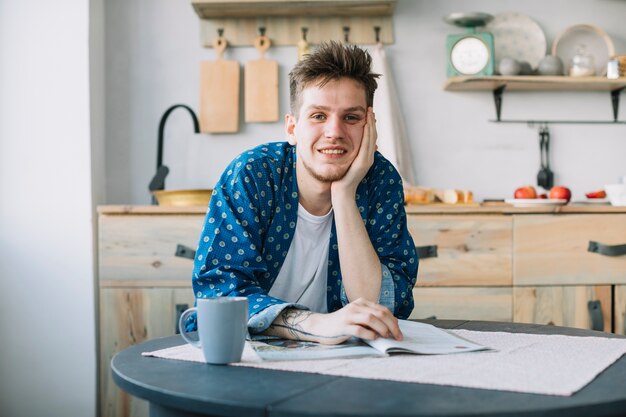 Front view of smiling man looking at camera with magazine and cup of coffee