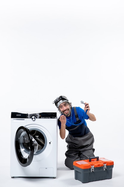 Free photo front view of smiling repairman holding stethoscope sitting near washing machine on wall