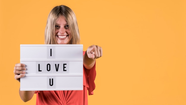 Front view smiling woman holding light box with i love u text against yellow surface