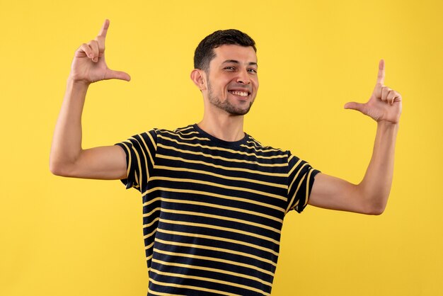 Front view smiling young man in black and white striped t-shirt standing on yellow isolated background