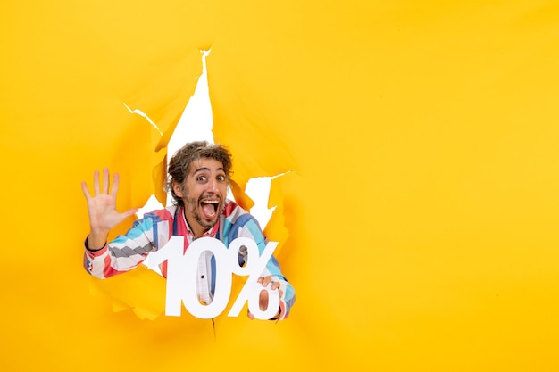 Free photo front view of smiling young man holding ten percentage and showing five in a torn hole in yellow paper