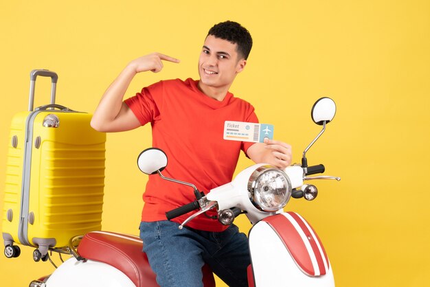 Front view smiling young man on moped holding ticket on yellow background