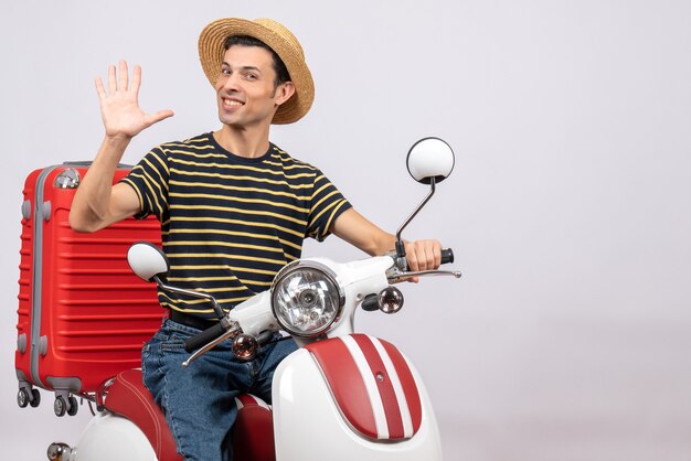 Front view of smiling young man with straw hat on moped waving hand