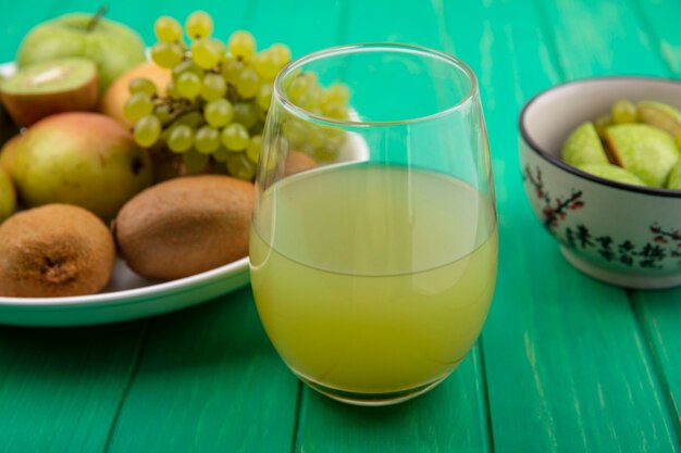 Front view soft drink in a glass with green apples  kiwi  green grapes and pear on a plate  on a green background