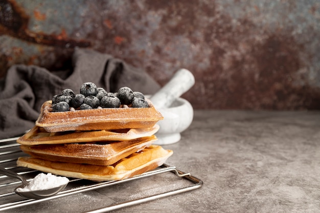 Free photo front view of stack of waffles with blueberries and powdered sugar