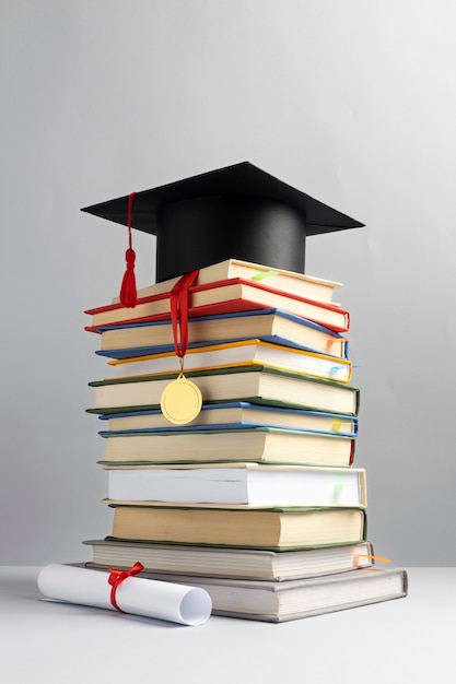 Front view of stacked books, a graduation cap and a diploma for education day