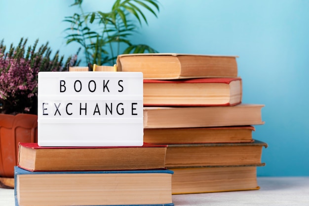 Free Photo front view of stacked books with pot of plants and light box