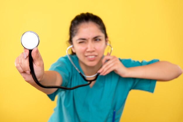 Front view of the stethoscope in femal doctor hand on yellow isolated wall