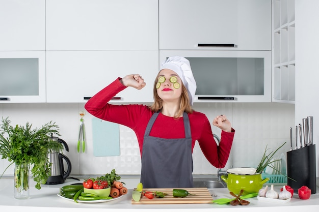 Front view streching female chef in uniform putting cucumber slices on her face