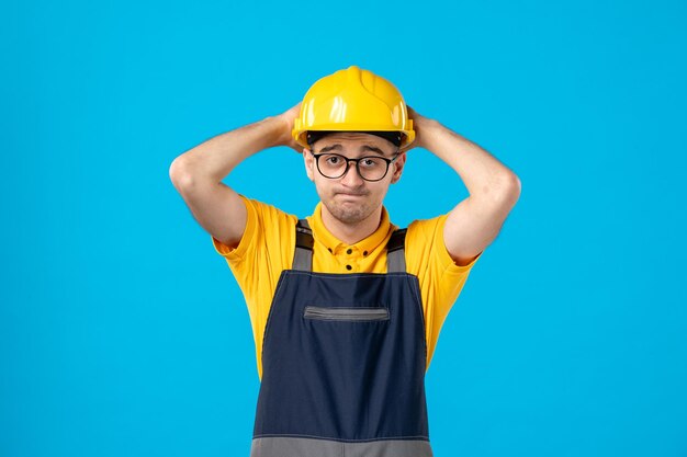 Front view of stressed male worker in uniform and helmet on a blue floor job handyman