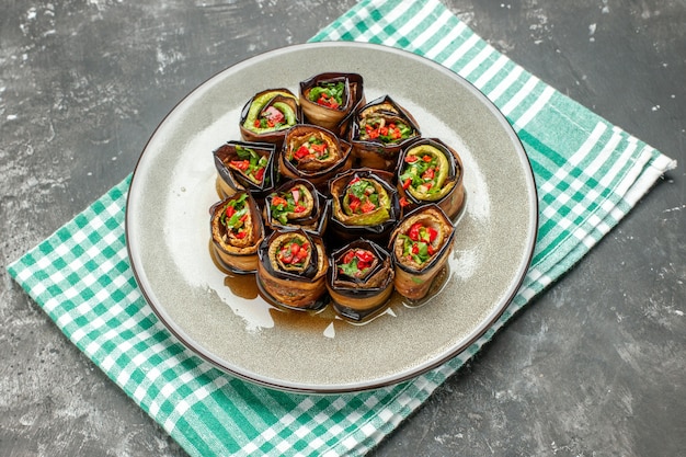 Front view stuffed aubergine rolls in oval plate turquoise-white tablecloth on grey background