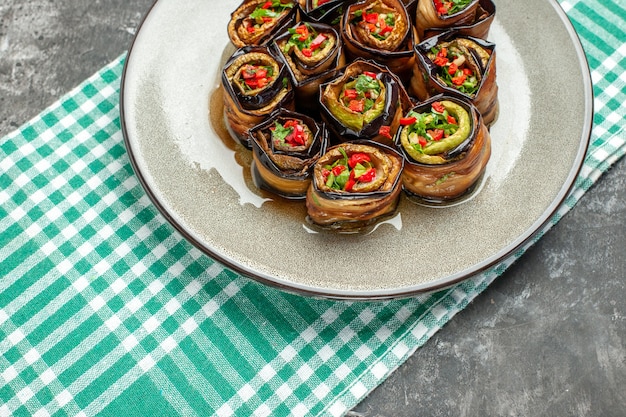 Front view stuffed aubergine rolls in white oval plate turquoise-white tablecloth on grey dish photo