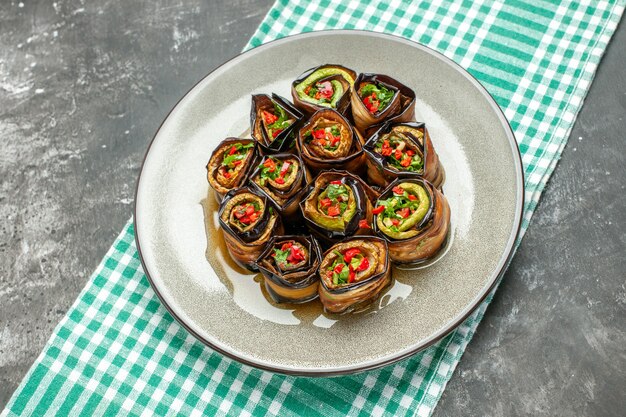 Front view stuffed aubergine rolls in white oval plate turquoise-white tablecloth on grey