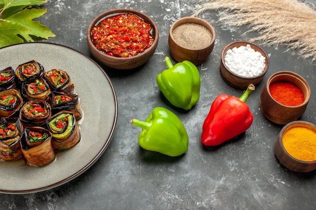 Free photo front view stuffed eggplant rolls spices in small bowls salt pepper red pepper turmeric adjika peppers on grey background