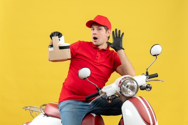 Front view of surprised courier man wearing red blouse and hat gloves in medical mask delivering order sitting on scooter holding orders showing five