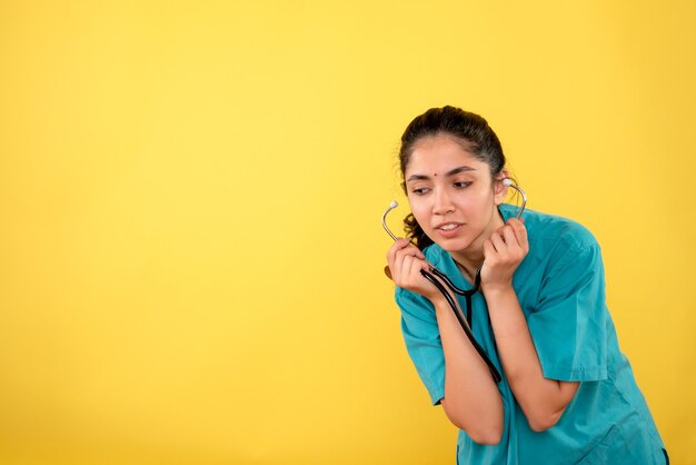 Front view surprised woman doctor in uniform holding stethoscope on yellow background