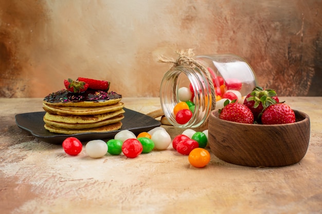 Front view sweet pancakes with colorful candies on light desk