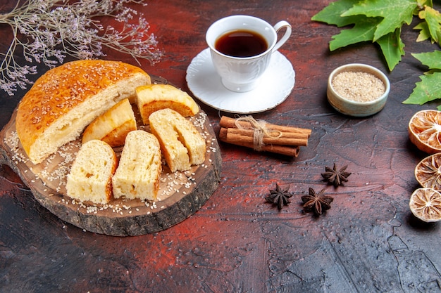 Front view sweet pastry sliced in pieces with cup of tea on dark background