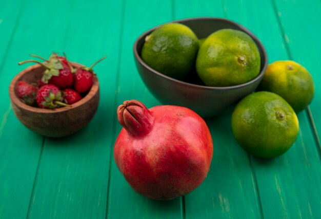 Front view tangerines in a bowl and pomegranate with strawberries on a green wall