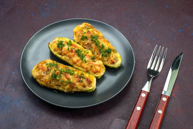 Front view tasty baked squashes with greens inside plate on the dark background.