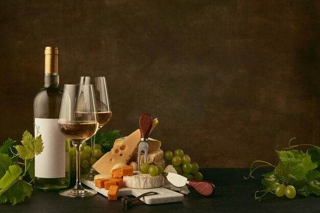 Front view of tasty cheese plate with grapes and the wine bottle, fruit and wineglasses