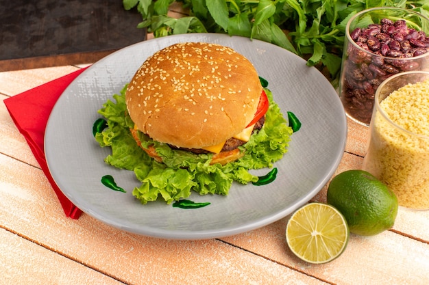 Front view tasty chicken sandwich with green salad and vegetables inside plate on the wooden cream desk.