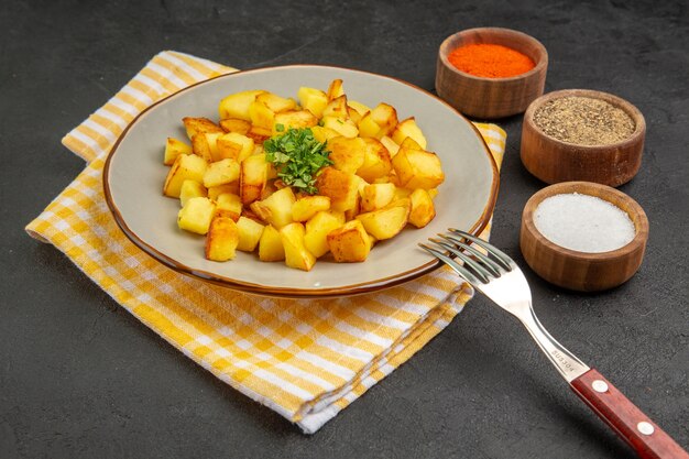 Front view tasty fried potatoes inside plate with seasonings on a dark-grey table