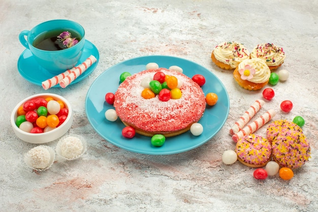 Front view tasty pink cake with yummy cookie cakes and tea on white background goodie rainbow candy dessert color cake