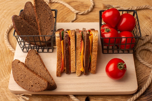 Front view tasty toast sandwich with cheese ham along with red tomatoes bread loafs on wooden desk