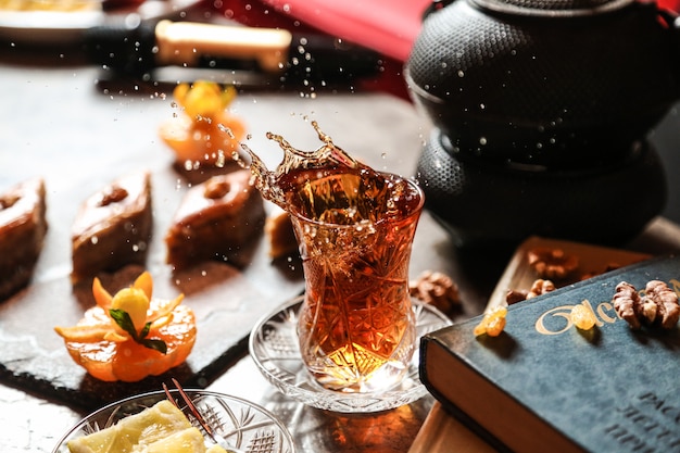 Front view tea in armudu glass with baklava and a book on the table