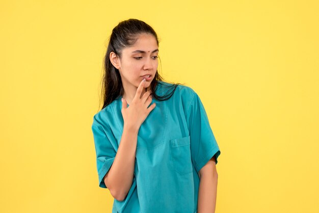 Front view thoughtful pretty female doctor standing on yellow background