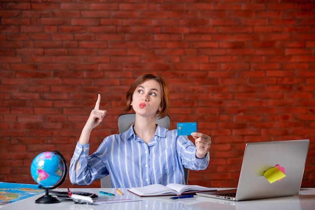 Front view travel agent behind her working place holding credit card map indoors manager operator worker agency occupation document money world