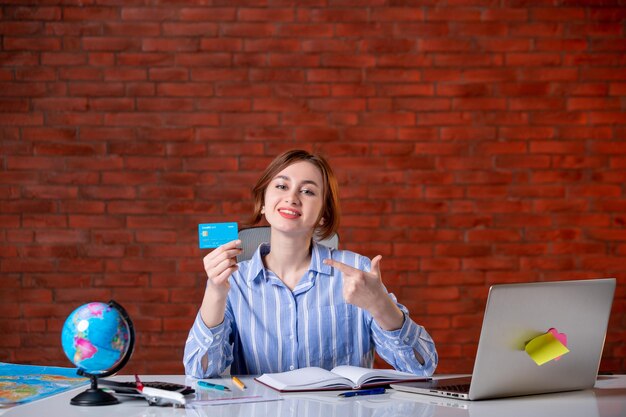 Front view travel agent behind her working place holding credit card map indoors manager worker service agency operator world occupation money document