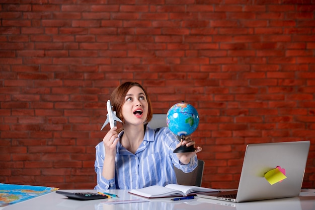 Free photo front view travel agent behind her working place holding little globe and toy plane map assistant agency indoors operator service manager